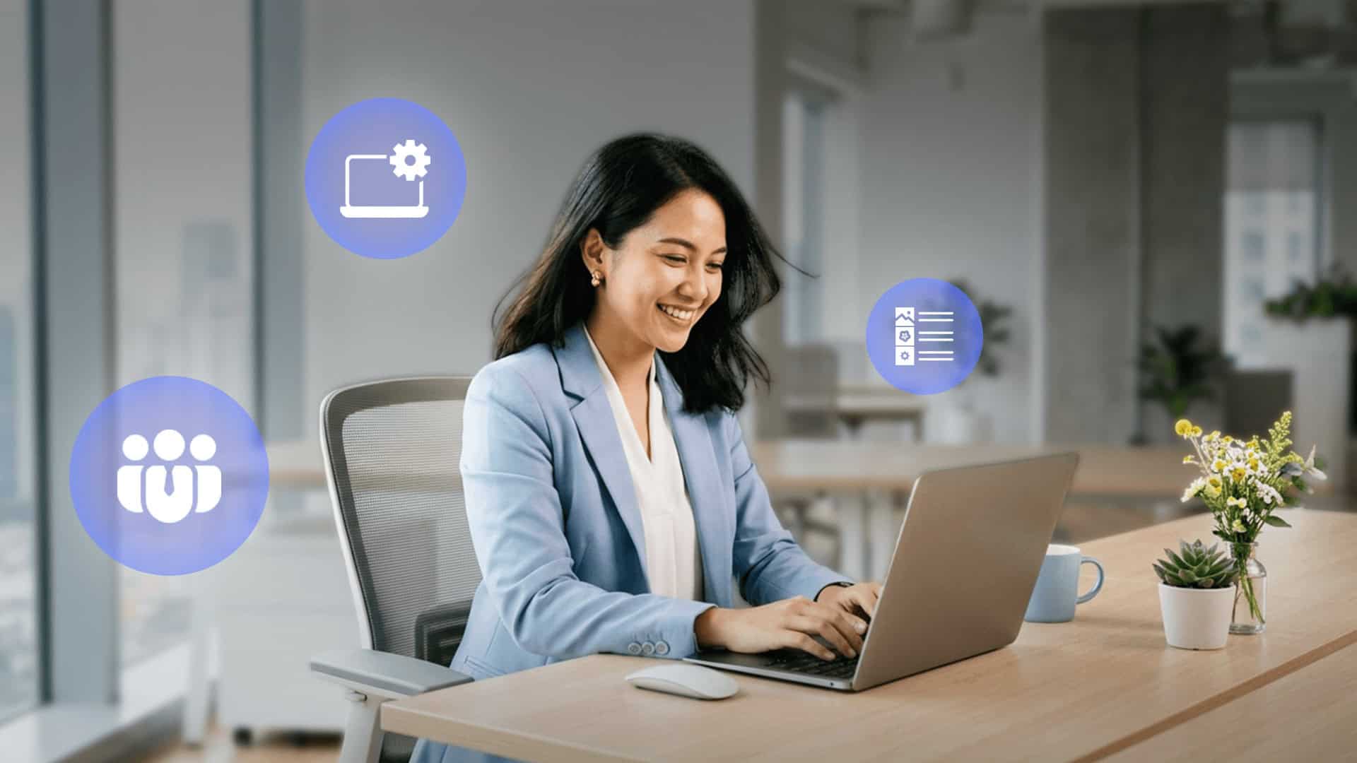 Seorang wanita berjas biru tersenyum sambil bekerja menggunakan laptop di meja kantornya.
