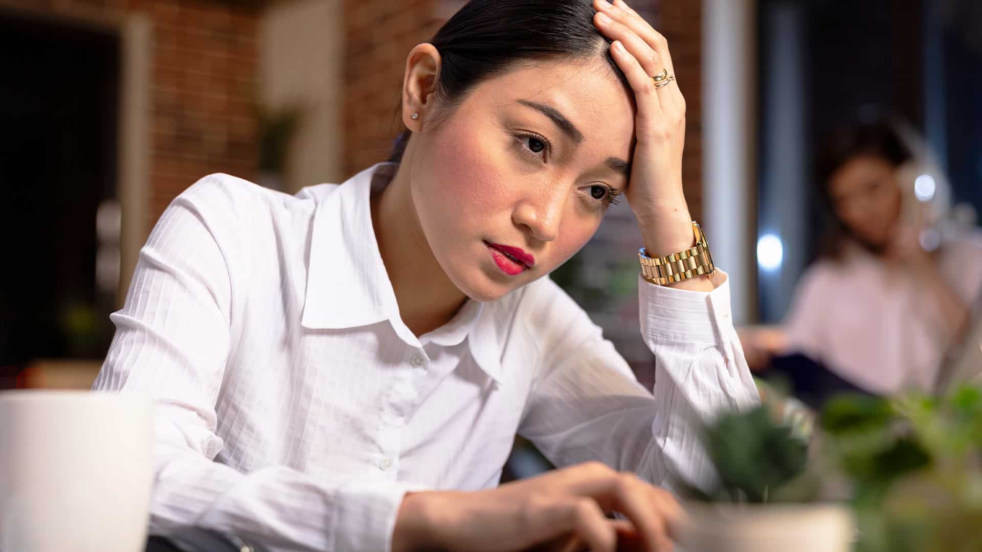 Seorang wanita bermuka lelah memegang dahi saat bekerja di depan laptop di kantor.