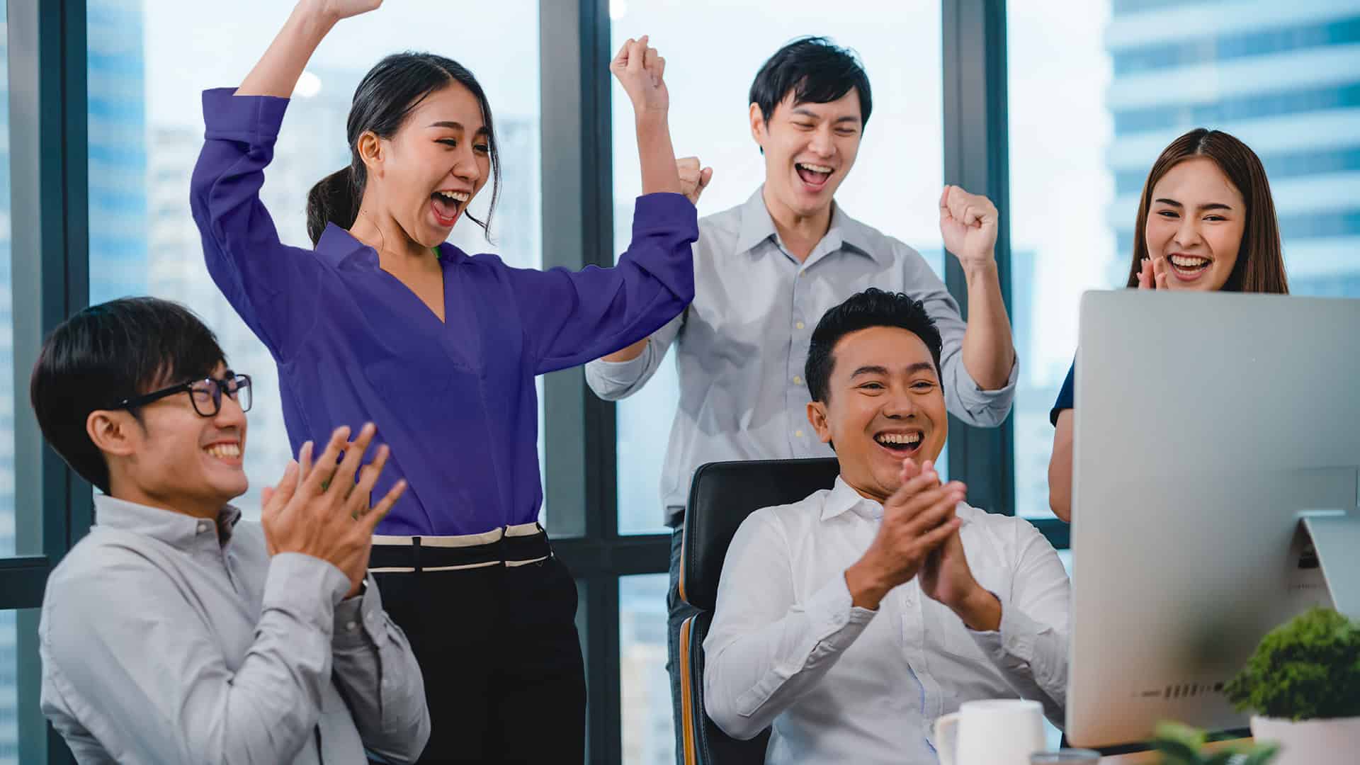 Sebuah tim kantor bersorak dan bertepuk tangan gembira di depan layar komputer